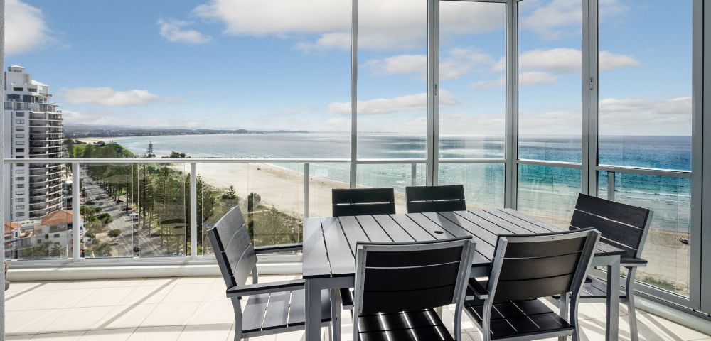 Elevated balcony view of the ocean with outdoor seating and a glass railing.