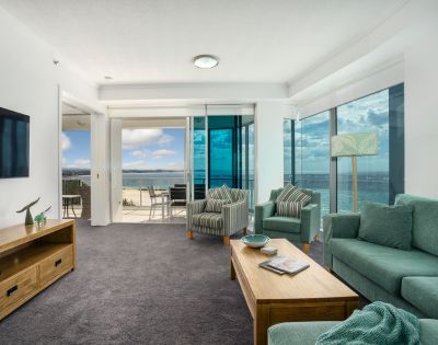 Living room with a large sofa and coffee table, featuring an ocean view through large windows.