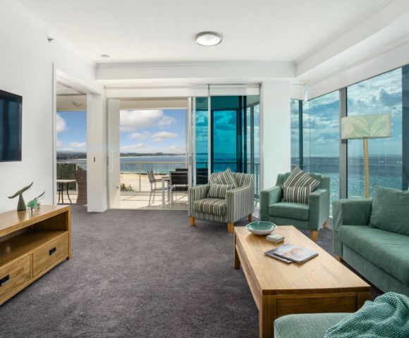 Living room with a large sofa and coffee table, featuring an ocean view through large windows.