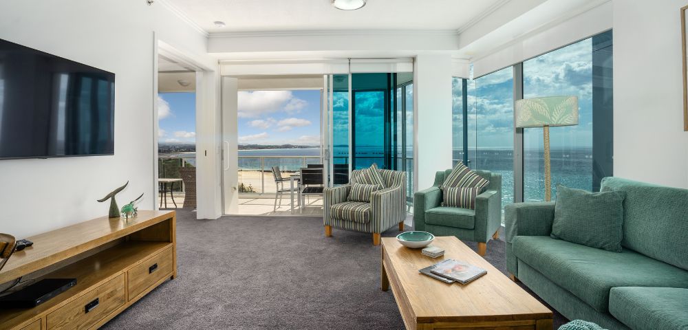 Living room with a large sofa and coffee table, featuring an ocean view through large windows.