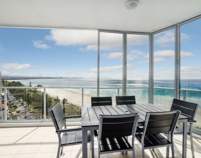 Elevated balcony view of the ocean with outdoor seating and a glass railing.