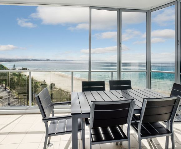 Elevated balcony view of the ocean with outdoor seating and a glass railing.