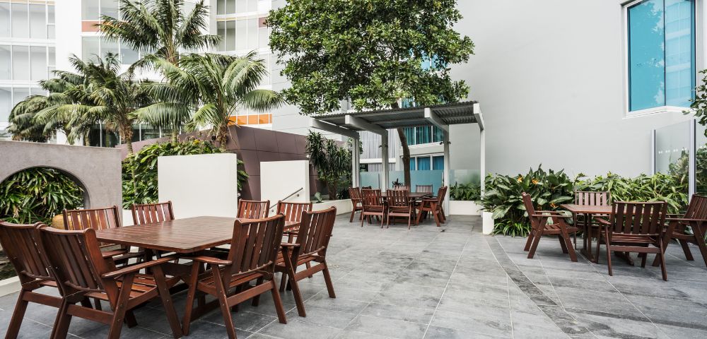 Outdoor dining area surrounded by greenery, with multiple tables and chairs for al fresco dining.