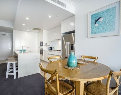 Dining area with a wooden table and chairs, adjacent to a kitchen with modern appliances.