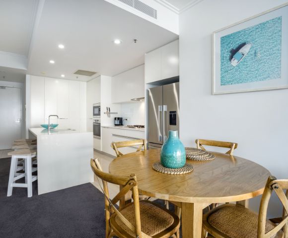 Dining area with a wooden table and chairs, adjacent to a kitchen with modern appliances.