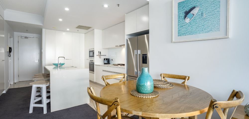Dining area with a wooden table and chairs, adjacent to a kitchen with modern appliances.
