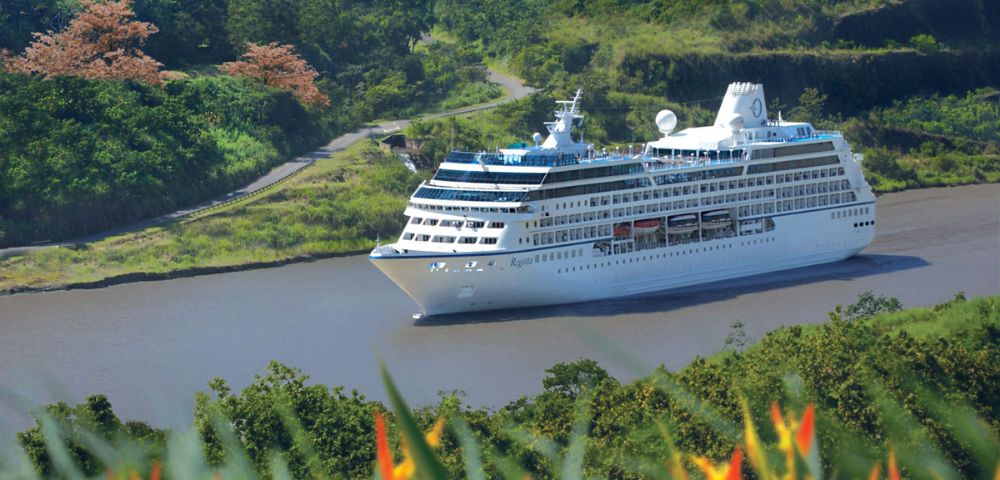 A luxurious cruise ship, Oceania Regatta, navigates the serene Panama Canal surrounded by lush greenery and tropical flowers in a vibrant natural setting.