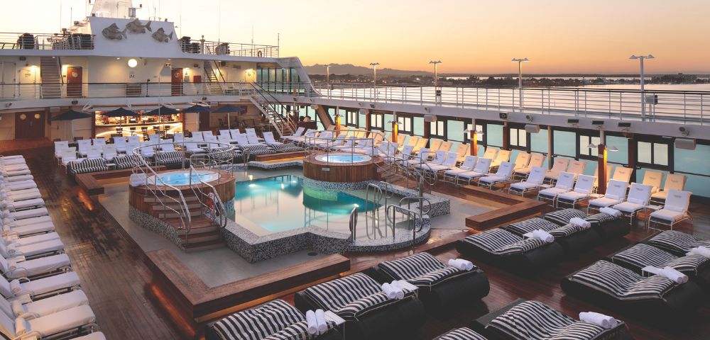 Oceania Regatta cruise deck at sunset featuring pools, hot tubs, and lounge chairs, with scenic ocean views and modern amenities.