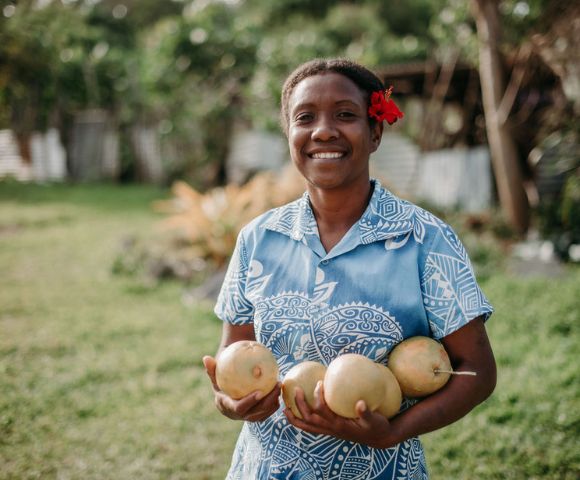 Person holding coconuts and smiling in a grassy area, adding a friendly and welcoming vibe to the resort experience.