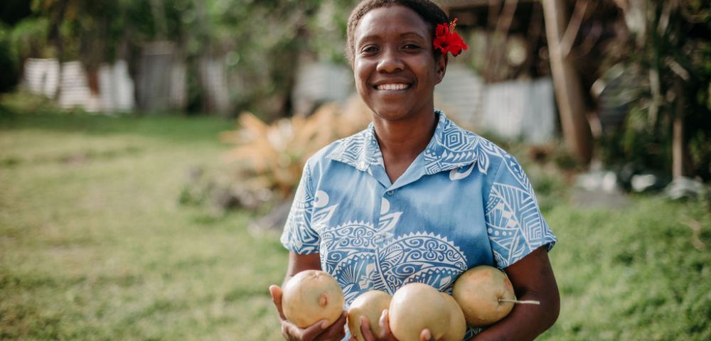 Person holding coconuts and smiling in a grassy area, adding a friendly and welcoming vibe to the resort experience.