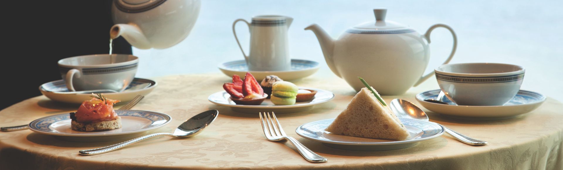 A waiter pours tea into a cup, surrounded by elegant pastries and a scenic ocean view.