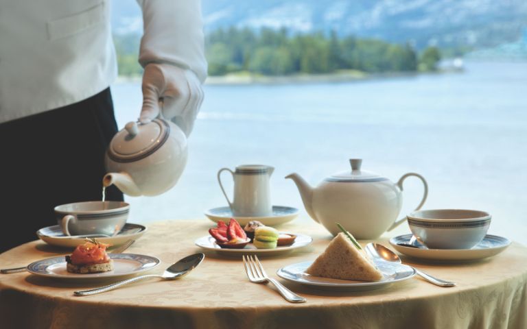 A waiter pours tea into a cup, surrounded by elegant pastries and a scenic ocean view.