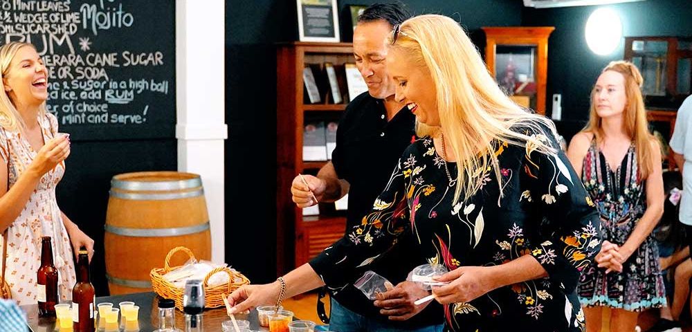 Group of people at a distillery or brewery with barrels in the background, watching someone pour drinks for tasting.