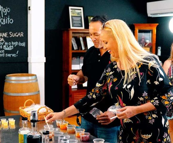 Group of people at a distillery or brewery with barrels in the background, watching someone pour drinks for tasting.
