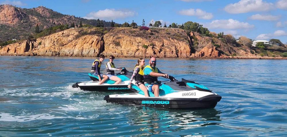 Two people each riding their own jet skis near rocky cliffs under clear skies.