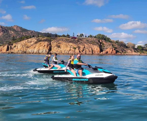 Two people each riding their own jet skis near rocky cliffs under clear skies.