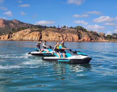 Two people each riding their own jet skis near rocky cliffs under clear skies.