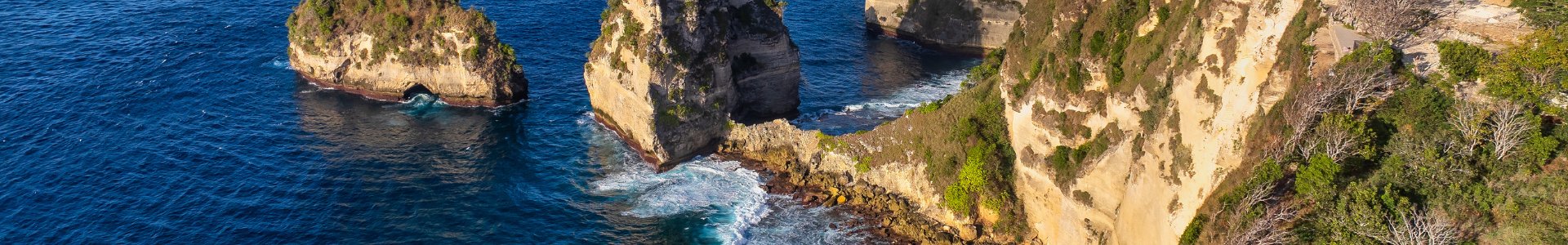 This stunning aerial image captures a pristine tropical beach nestled between towering, lush green cliffs that plunge dramatically into the turquoise ocean. The golden sandy shoreline curves gently, inviting relaxation amidst the vibrant blue waters that sparkle under a clear sky. The scene exudes tranquility and natural beauty, showcasing a breathtaking coastal paradise perfect for unwinding and exploring.