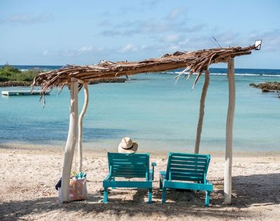 Idyllic beach scene with clear blue water, white sand, and lounge chairs under a wooden canopy.
