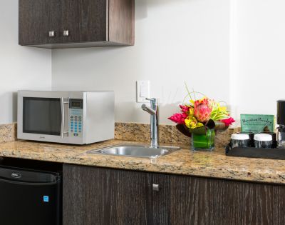 Hotel room kitchenette with granite countertop, microwave, coffee maker, and a vase with flowers.