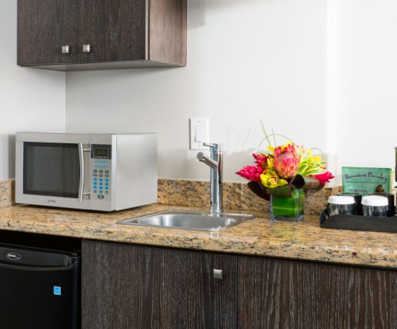 Hotel room kitchenette with granite countertop, microwave, coffee maker, and a vase with flowers.