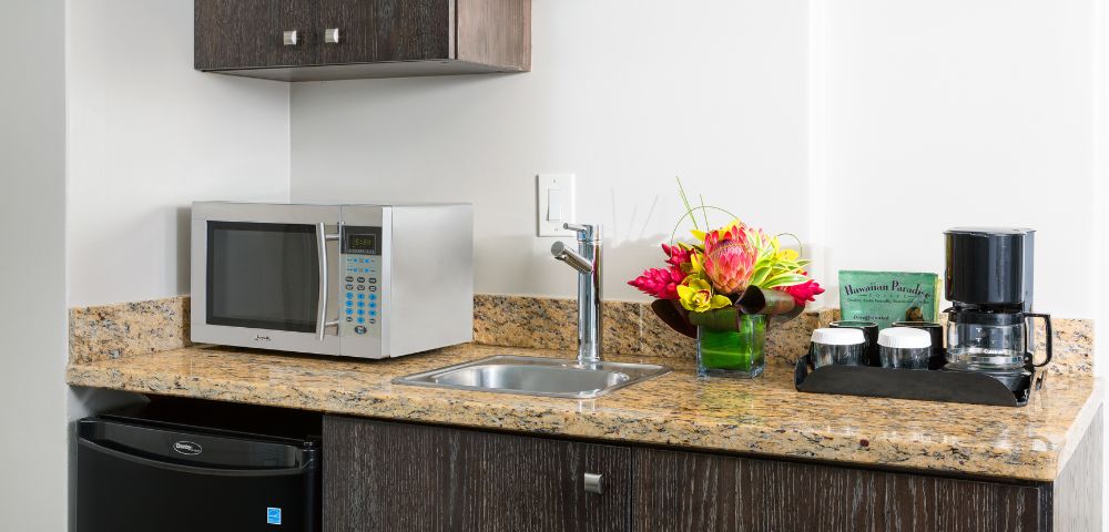 Hotel room kitchenette with granite countertop, microwave, coffee maker, and a vase with flowers.