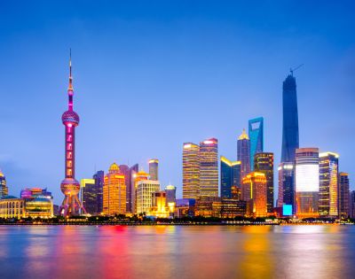 Shanghai skyline at dusk, featuring illuminated skyscrapers reflected in the calm river. The scene conveys a vibrant, futuristic cityscape.