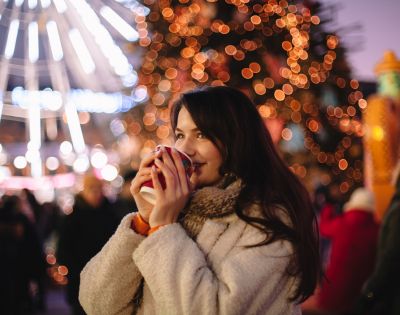 A woman enjoy hot drinks at an outdoor Christmas market.