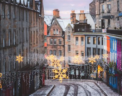 A festive street in Edinburgh, Scotland is adorned with Christmas lights and historic architecture.