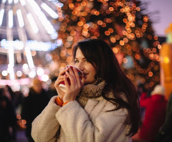 A woman enjoy hot drinks at an outdoor Christmas market.