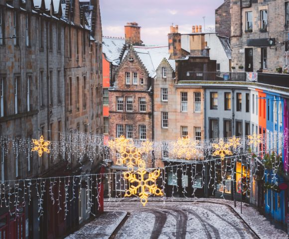 A festive street in Edinburgh, Scotland is adorned with Christmas lights and historic architecture.