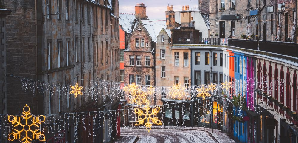 A festive street in Edinburgh, Scotland is adorned with Christmas lights and historic architecture.