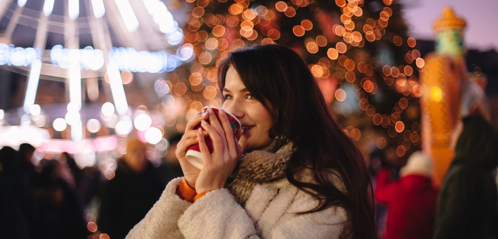 A woman enjoy hot drinks at an outdoor Christmas market.
