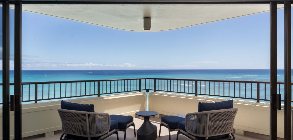 Outdoor balcony with seating, offering panoramic views of the ocean at the Moana Surfrider resort.