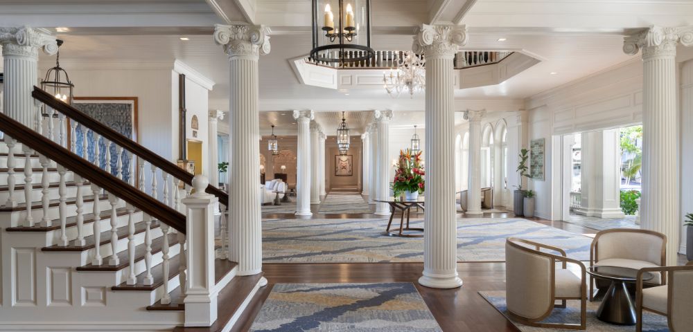 Elegant lobby view featuring a grand staircase with dark wood railings, white steps, and stylish seating at the Moana Surfrider, A Westin Resort in Hawaii.