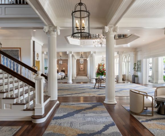 Elegant lobby view featuring a grand staircase with dark wood railings, white steps, and stylish seating at the Moana Surfrider, A Westin Resort in Hawaii.
