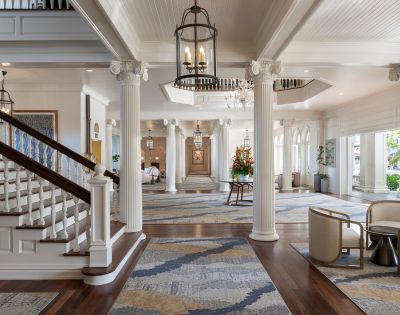 Elegant lobby view featuring a grand staircase with dark wood railings, white steps, and stylish seating at the Moana Surfrider, A Westin Resort in Hawaii.