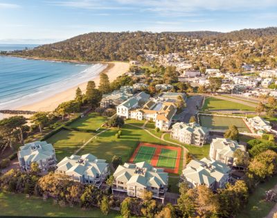 Aerial view of a coastal town featuring sandy beaches, residential buildings, and recreational areas including tennis courts.