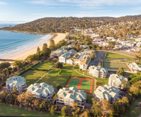 Aerial view of a coastal town featuring sandy beaches, residential buildings, and recreational areas including tennis courts.