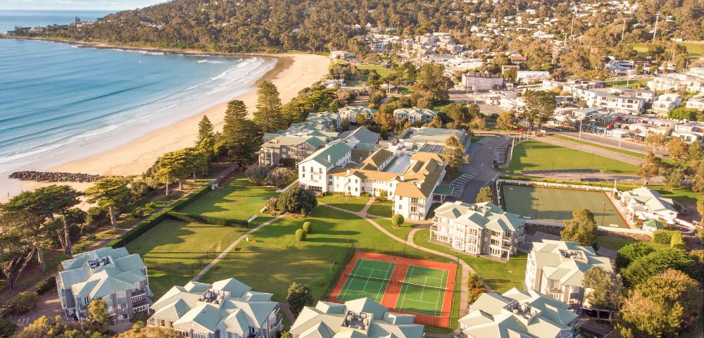 Aerial view of a coastal town featuring sandy beaches, residential buildings, and recreational areas including tennis courts.