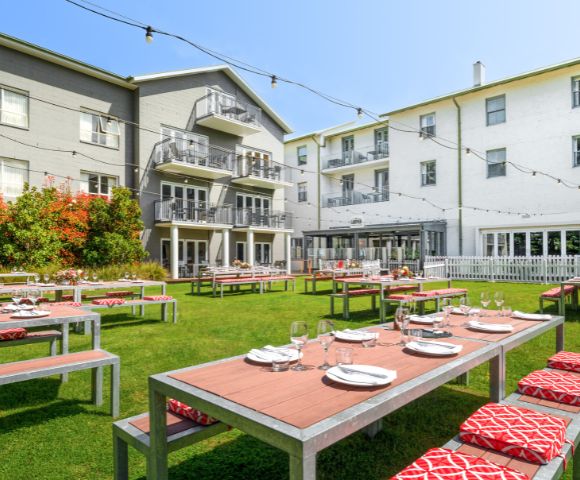 Outdoor dining area in front of a hotel or large building, with tables set for dining and greenery surrounding the space.