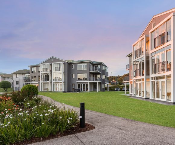 Exterior view of residential buildings during sunset or sunrise, with landscaped gardens and warm lighting.