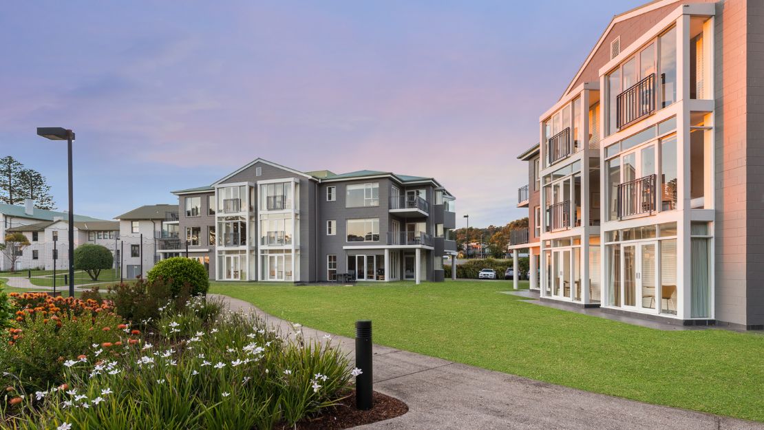 Exterior view of residential buildings during sunset or sunrise, with landscaped gardens and warm lighting.