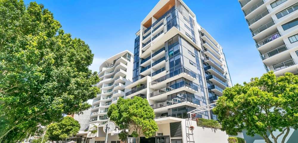 Exterior view of a modern multi-story residential building with balconies, large windows, and surrounding greenery.