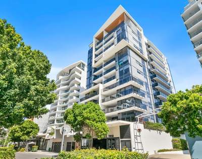 Exterior view of a modern multi-story residential building with balconies, large windows, and surrounding greenery.