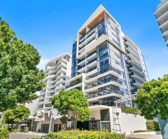 Exterior view of a modern multi-story residential building with balconies, large windows, and surrounding greenery.