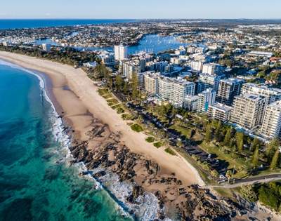 Aerial view of a sandy beach with clear blue water and numerous buildings along the coast.