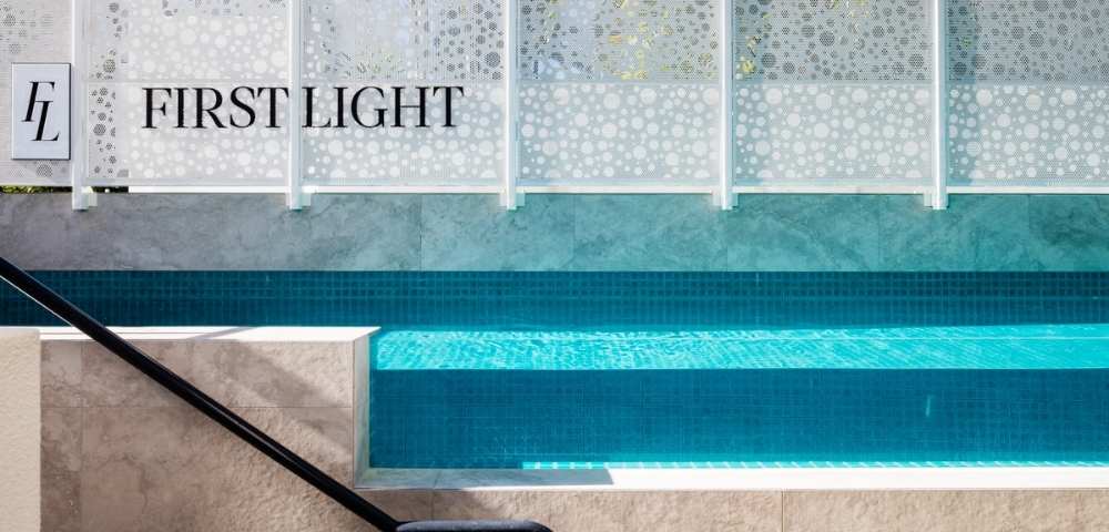 Close-up view of a swimming pool with clear water and steps, adjacent to a wall labeled 'FIRST LIGHT'.