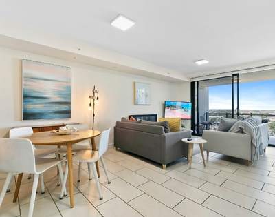 Open-plan living area with a dining table, chairs, sofa set, TV, and large windows providing an expansive outdoor view.