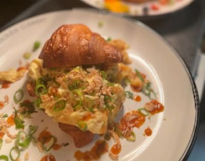 Close-up of a plated dish featuring a pastry or croissant topped with savory ingredients like green onions and possibly seafood.